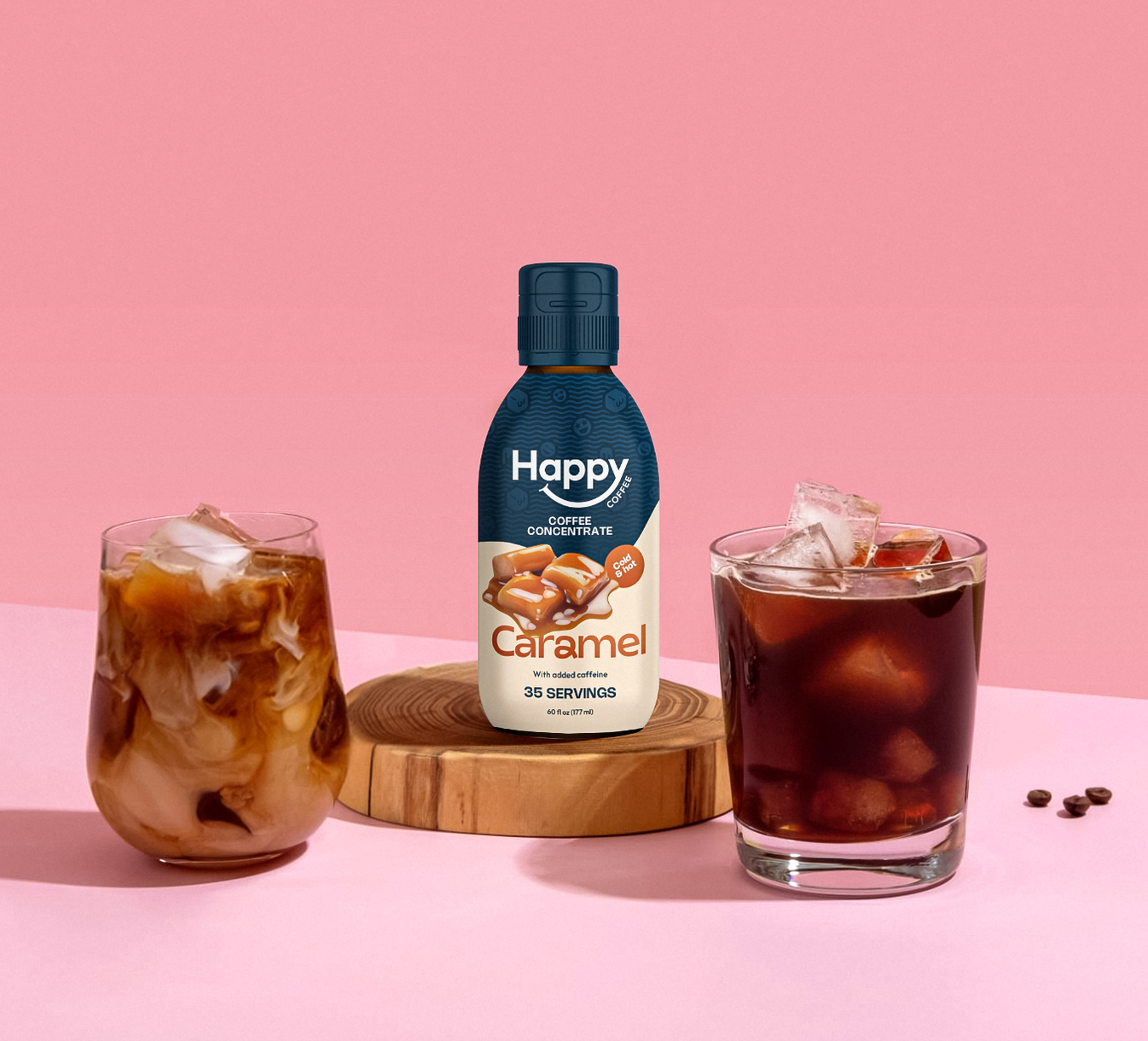 A bottle of Happy Coffee Caramel Concentrate with two glasses of iced coffee on a pink background.
